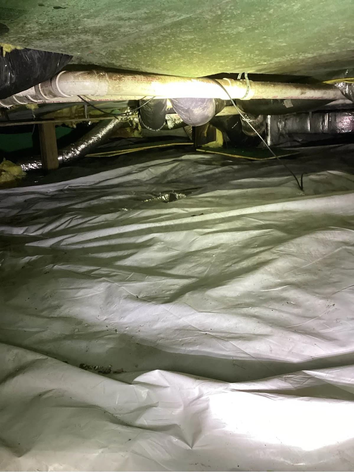 Vapor barrier laid across a crawlspace floor beneath a home, ductwork and plumbing overhead