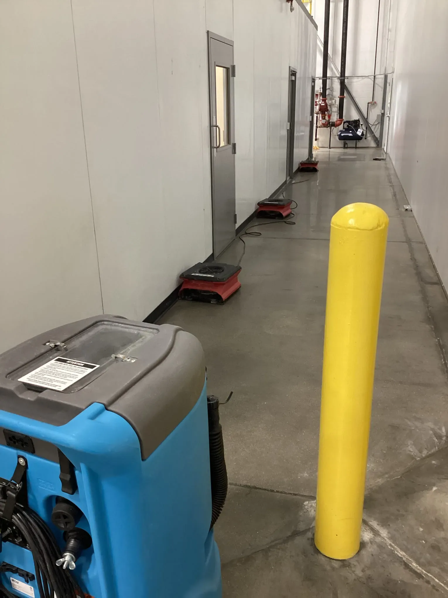 Commercial dehumidifier running on a flooded warehouse floor beside a safety bollard