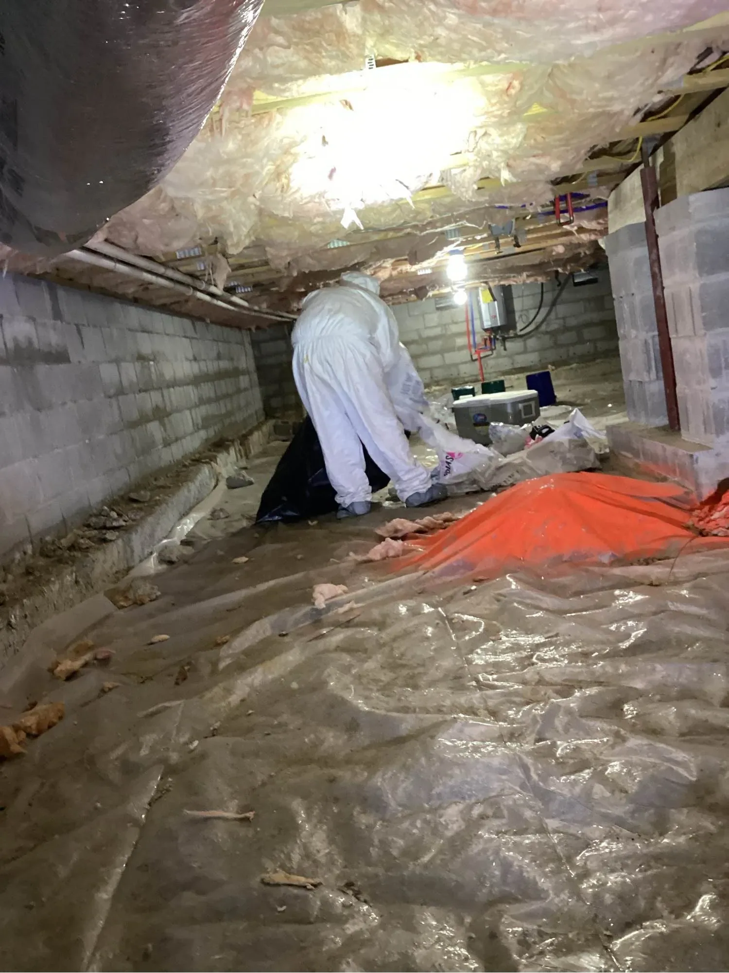 Technician in protective coveralls working on a vapor barrier inside a crawl space