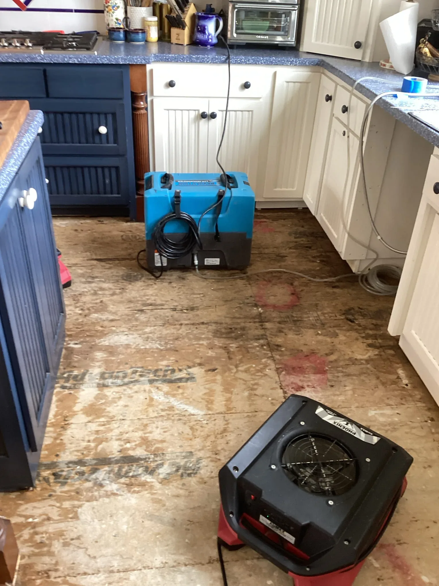Kitchen with the flooring removed to the subfloor, a commercial dehumidifier and air mover drying it after a water emergency