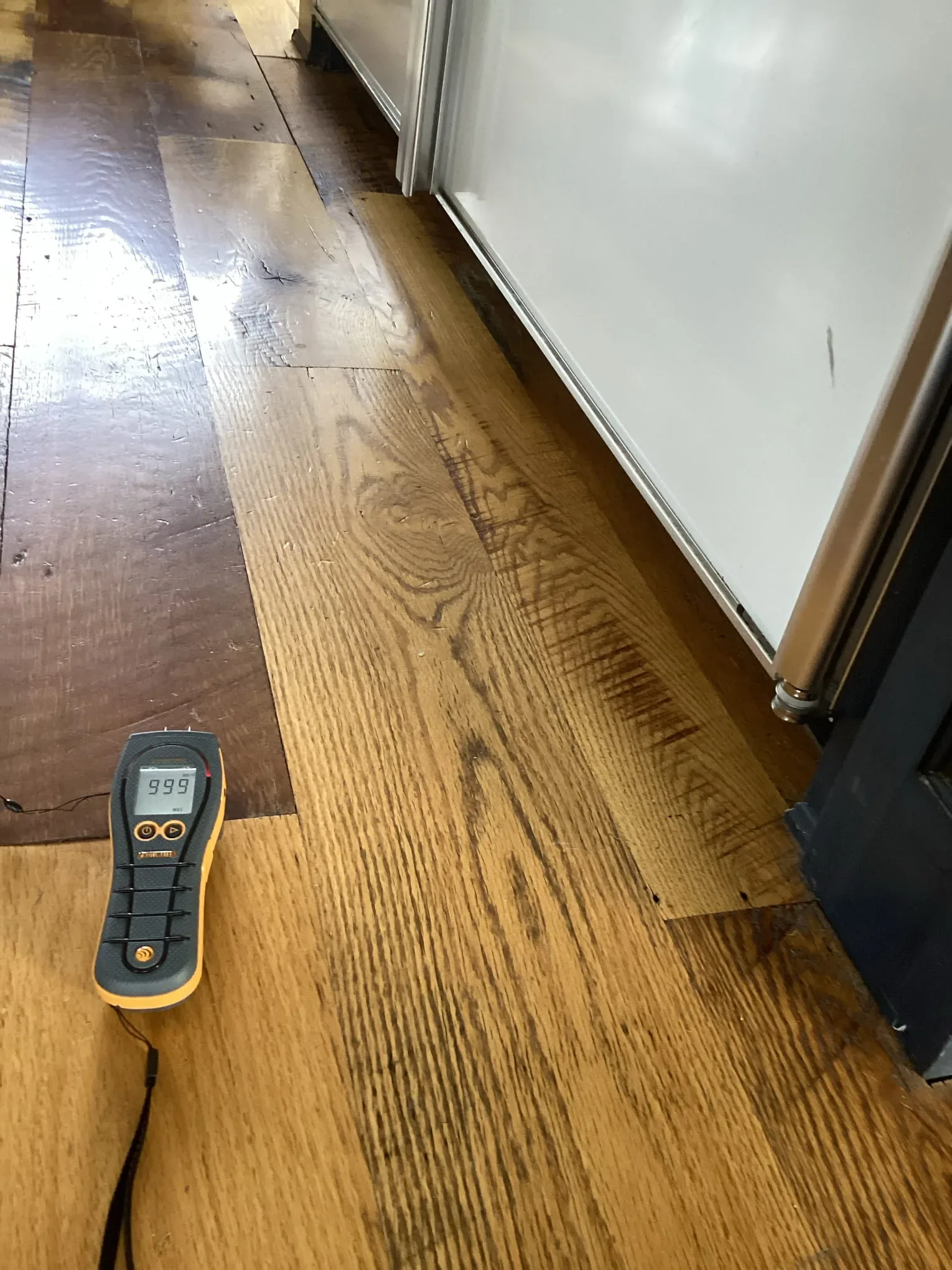 Moisture meter resting on a hardwood floor during drying