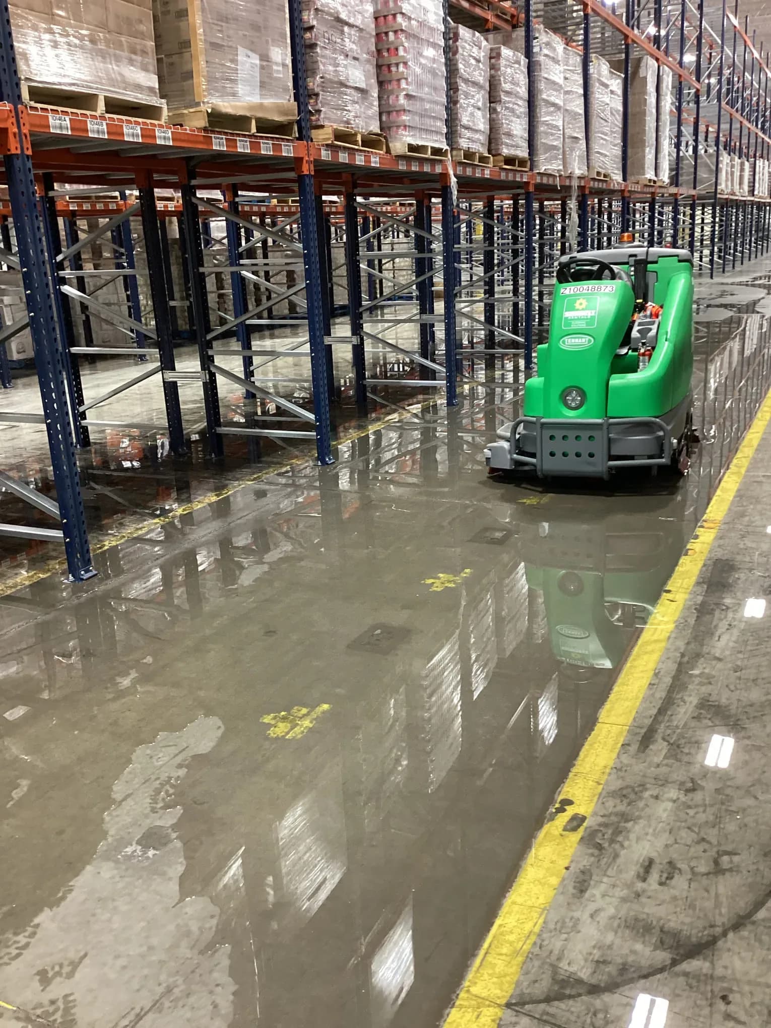 Floor scrubber extracting standing water from a flooded warehouse floor beside pallet racking