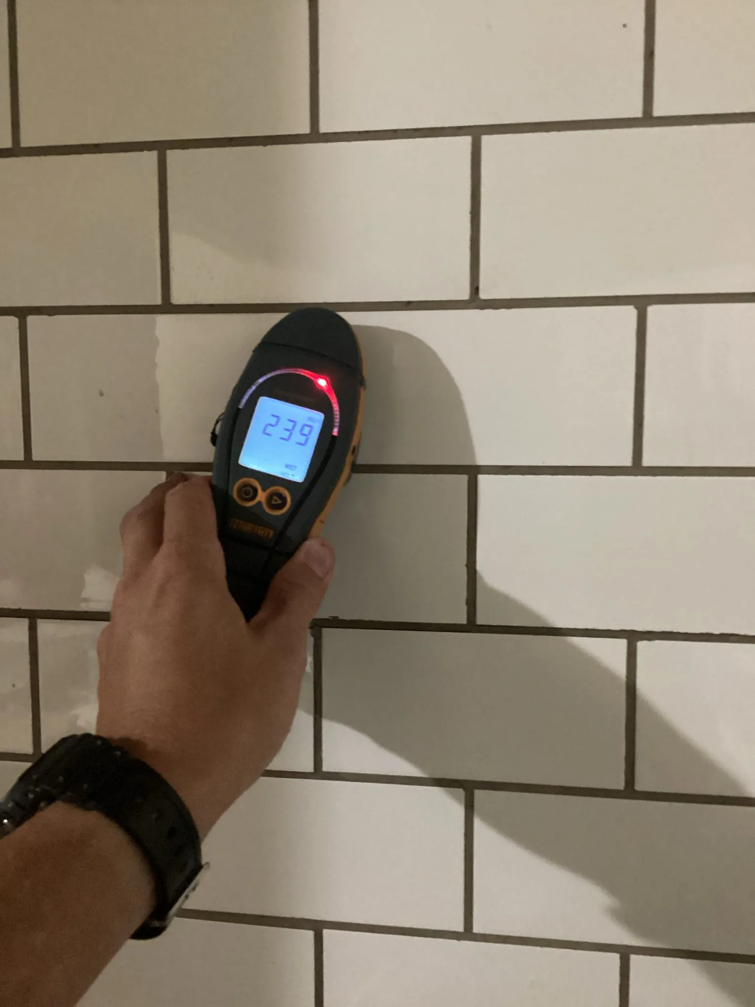 Moisture meter reading being taken on a tiled surface to trace the moisture source feeding mold growth