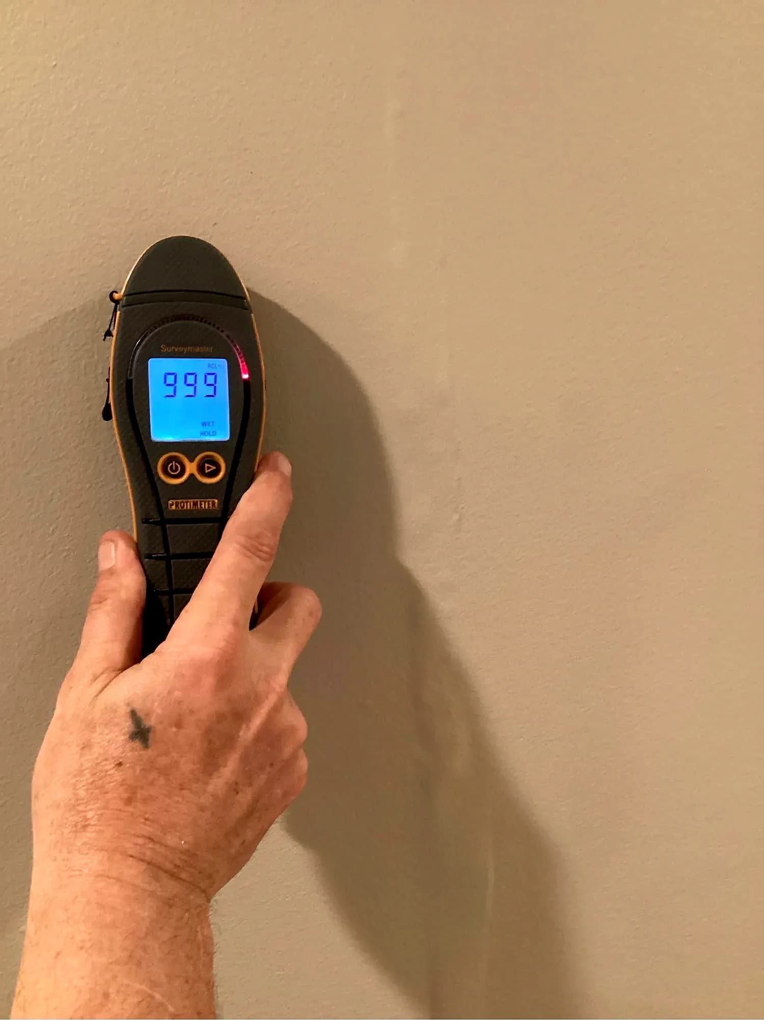 Moisture meter pressed against a wall to locate hidden water intrusion behind the surface