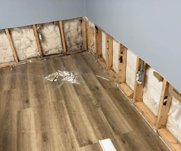 Drywall cut back to the studs along the base of a wall after a water loss, with the flooring left in place