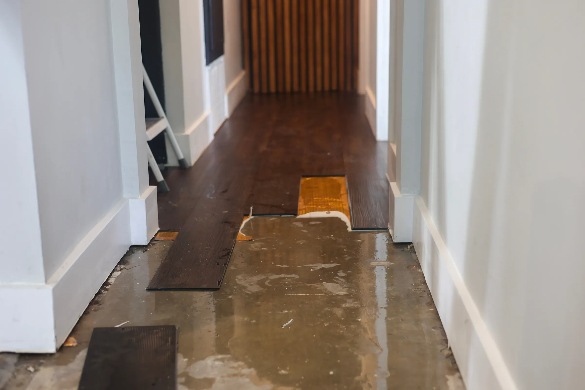 Standing water across a home hallway floor after a slab leak, with flooring planks lifted