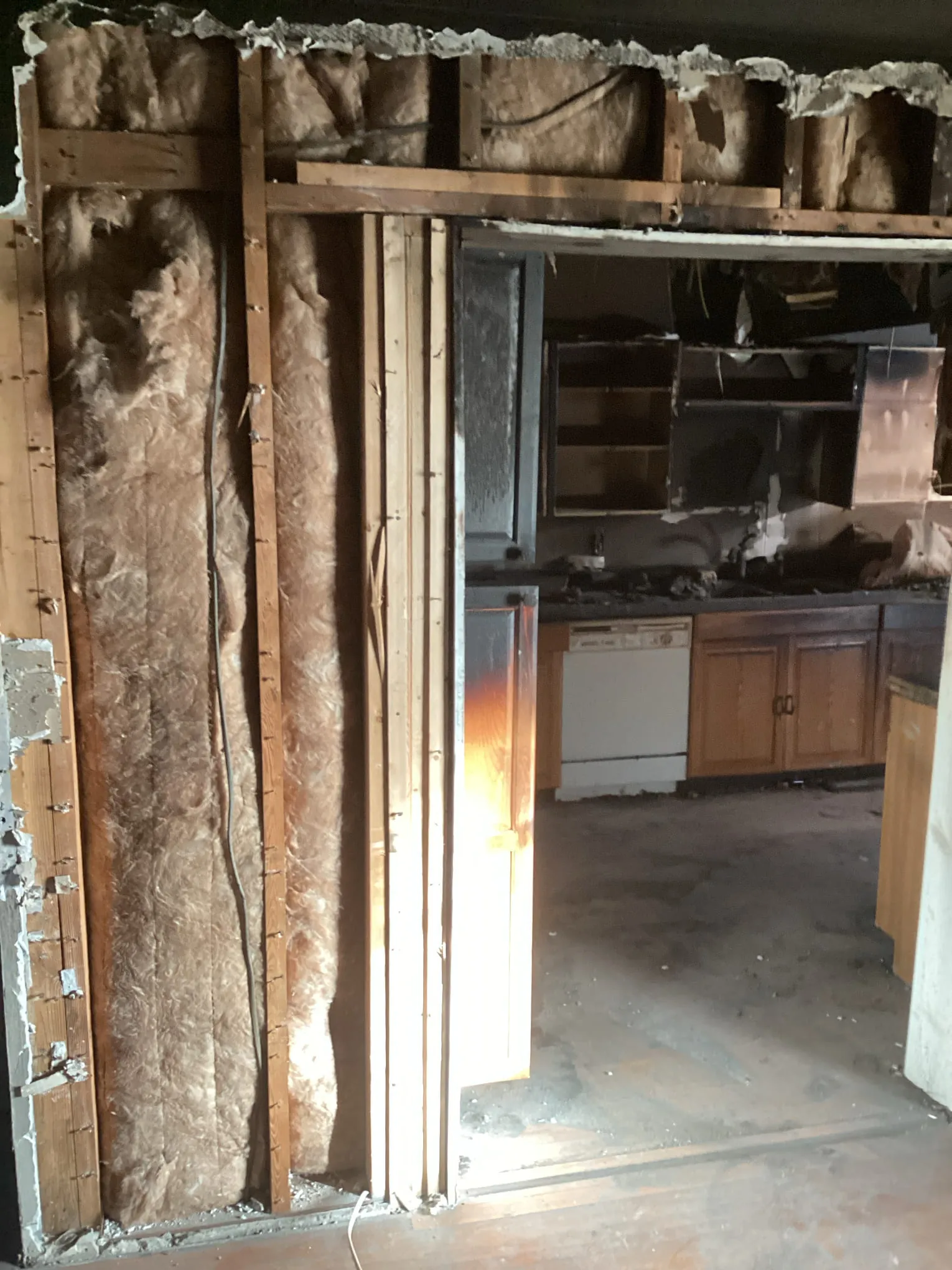 Kitchen wall opened to the framing beside fire damaged cabinets during a cleanup